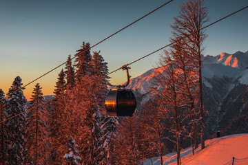 A gondola and ski lift against the backdrop of a winter landscape of mountains, trees, and an evening sunset in Krasnaya Polyana.