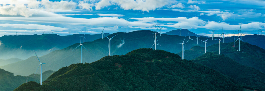 A large wind farm with modern wind turbines on the green mountain for renewable electricity generation under a blue sky