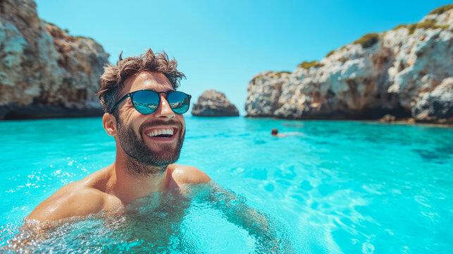Joyful man in sunglasses smiling happily in crystal clear turquoise sea water surrounded by beautiful rocky cliffs on sunny summer day