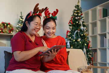 Festive Moments. Two friends sharing laughter over a tablet during the holiday season.