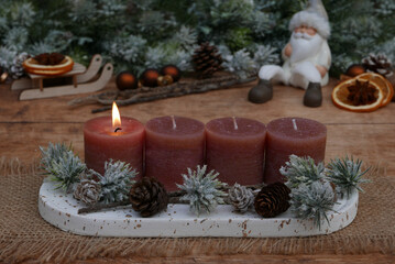 Erster Advent: Adventsdekoration vor weihnachtlicher Kulisse, mit braunen Kerzen eine davon brennt zum 1. Advent.