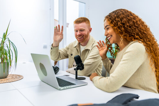 Diverse couple recording podcast, streaming video call, waving at laptop