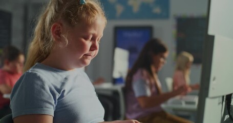 Close up of Focused European Schoolgirl Using Computer in Modern Classroom. Other Children Study in Background. Concept of Digital Education, Childhood Learning, and Technology In Schools. Handheld. - Powered by Adobe
