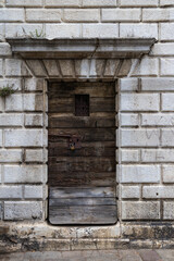 Fototapeta premium Close-up of an old weathered wooden door with a rusty metal lock and padlock set in a white stone wall. Vintage architecture detail with texture and history.