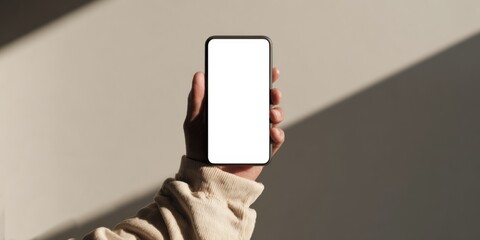 Raised hand holding smartphone with blank screen on beige background.