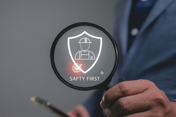 Businessman holds a magnifier over a Safety First shield icon. A concept of workplace security, risk management, and compliance with industry regulations, ensuring employee protection and insurance.