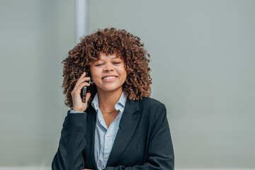 young businesswoman with afro hair and a mobile phone smiling on the street