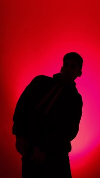 A man in a hoodie performs modern street dance as a clean silhouette against a vivid red magenta gradient in a minimalist studio