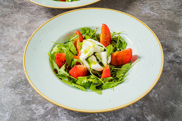 A vibrant salad featuring creamy burrata, juicy tomatoes, and fresh arugula on a light plate