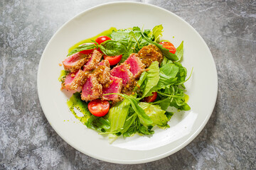 A colorful salad features seared tuna, fresh greens, and cherry tomatoes drizzled in dressing
