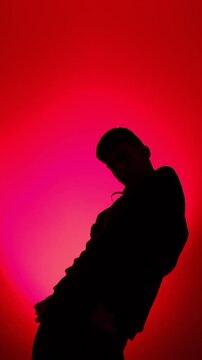 A man in a hoodie performs modern street dance against a vivid red gradient background, lit to a clean silhouette in a minimalist studio, filmed in real time.