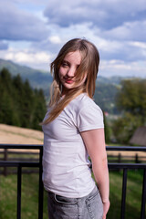A young teenage girl in a white T-shirt with her hair down. Against the background of mountains and sky.