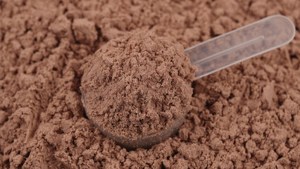 Scoop filled with chocolate protein powder. Close-up of sports nutrition supplement for fitness,...