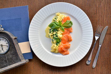 breakfast salmon with omelet on a white plate on a brown table with coffee