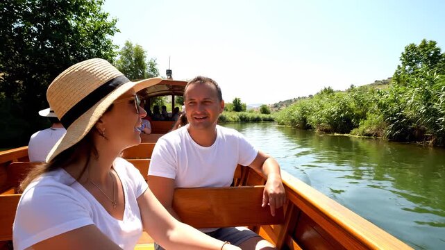 A man and woman sit on a boat, with the man and woman enjoying a peaceful trip under the sun. The boat glides quietly as the man and woman relax by the water's edge.