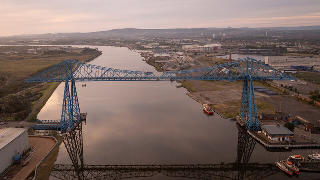 Aerial view of the iconic blue Transporter Bridge standing tall over the reflective River Tees, contrasting with the industrial landscape, Middlesbrough, England.