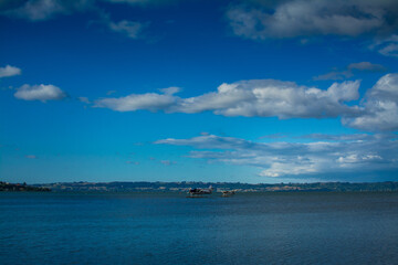 Fototapeta premium A pair of seaplanes rest on the calm waters of Lake Rotorua under dramatic storm clouds, ready for adventure against the rugged backdrop of New Zealand volcanic landscape and distant rolling hills.