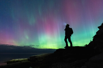 Silhouette of an adventurous hiker with a headlamp watching the magical Northern Lights, Aurora Borealis, over the Baltic Sea.