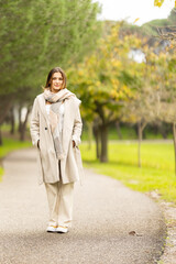 Woman smiling wearing long coat and scarf in park