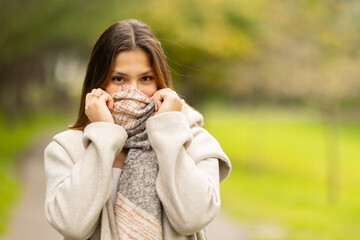 Fototapeta premium Shy young woman covering face with warm autumn scarf