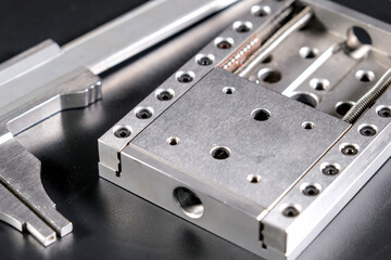 Close up of a precision linear motion guide rail with metal screws and a caliper on a black background.