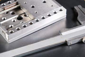 Close up of a precision linear motion guide rail with metal screws and a caliper on a black background.