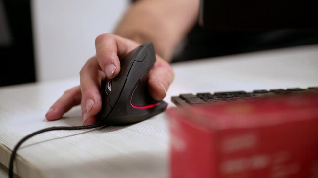 Close-up of a person's hand using an ergonomic vertical computer mouse next to a keyboard, conveying office work, technology, and business productivity