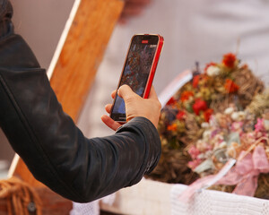Close-up of a visitor capturing decorated florist stall with smartphone at Naplavka farmers market in Prague, lifestyle and social media sharing.