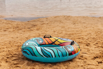 Naklejka premium A vibrant inflatable tube sits on golden sand, close to the water's edge. The sun shines brightly, promising a perfect day for swimming and relaxation at the beach