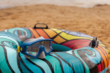Brightly colored swimming tube with a unique design rests on sandy beach. A pair of snorkeling goggles sits on top, ready for underwater exploration. The scene is peaceful and inviting