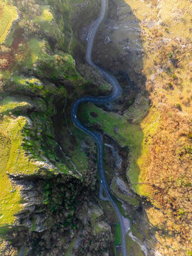 Aerial view of a winding road cutting through the vibrant green and brown hills of Cheddar Gorge, creating a striking contrast of color and texture, Cheddar, England, United Kingdom.