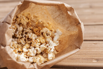 A brown paper bag filled with warm, freshly popped popcorn rests on a wooden surface. Perfect for a...