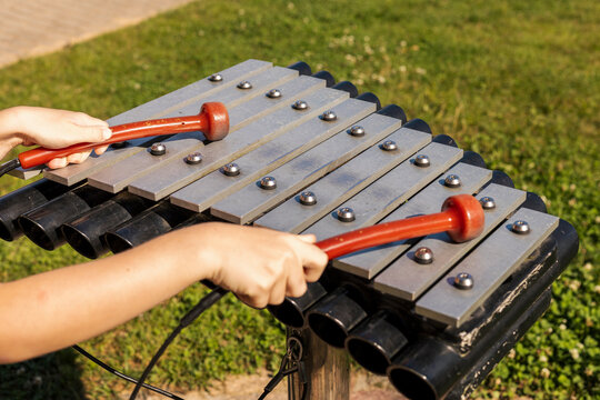 Two children play lively tunes on a vibrant outdoor xylophone in a sunny park setting. The grass is green and the atmosphere is cheerful, filled with the joy of music