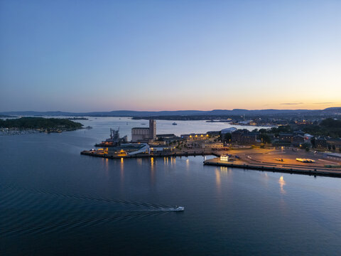 Aerial view of the tranquil waters reflecting the soft glow of harbor lights, juxtaposed against the silhouettes of the Akershus Fortress and Aker Brygge, Oslo, Oslo, Norway.