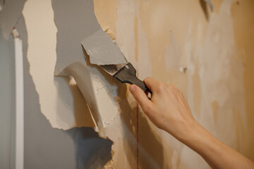 Hand scraping old wallpaper off wall