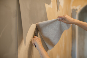 Person removing old wallpaper from home wall with scraper