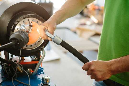 Worker crimping hydraulic hose on machine in workshop