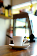 A white coffee cup sits on a saucer on a wooden table in a cafe.