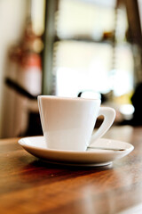 A white coffee cup and saucer sit on a wooden table in a cafe.