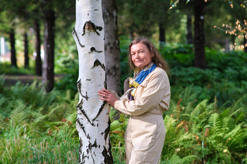 Woman touching birch tree trunk. Connection with nature concept. Outdoor healthy lifestyle. Middle-aged woman (50 years old)