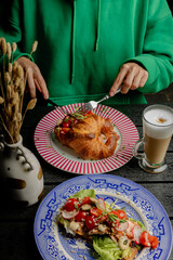 A girl cuts a croissant with filling with a knife and fork