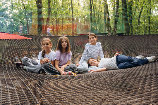 Fototapeta In casual clothes, relaxed, sitting. Kids are playing on the children's amusement ropes course