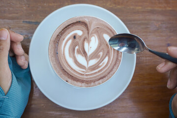 Cappuccino coffee with heart-shaped latte art on a wooden table, a close-up photo of a cappuccino drink in a white cup with a spoon on a wood background.