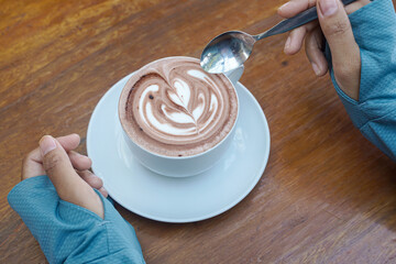Cappuccino coffee with heart-shaped latte art on a wooden table, a close-up photo of a cappuccino drink in a white cup with a spoon on a wood background.