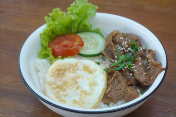 A vibrant bowl of rice topped with grilled beef, a fried egg, and colorful vegetables, served in a rustic dish