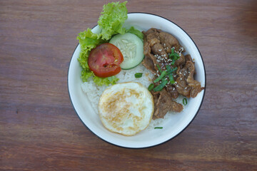 A vibrant bowl of rice topped with grilled beef, a fried egg, and colorful vegetables, served in a rustic dish