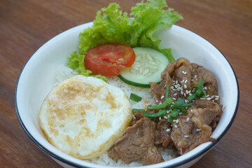 A vibrant bowl of rice topped with grilled beef, a fried egg, and colorful vegetables, served in a rustic dish