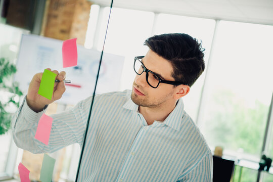Young professional businessman strategizing ideas using colorful post-it notes on a transparent board in a modern office setting