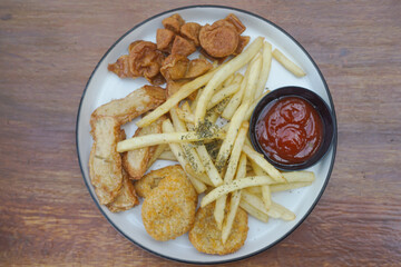 A delicious plate of golden fried snacks with ketchup and crispy fries on a wood background