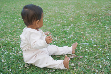 Adorable little baby sitting on green grass outdoors, closeup